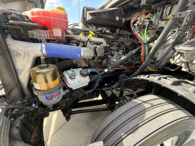 Freightliner PT126064S engine bay showing blue silicone hose, coolant reservoir, filter canister, and wiring harness inside cab-forward chassis.