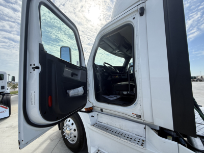 Truck cab doorway with open door, interior visible, step with metal tread, underside of cab, side mirror, and part of the steering wheel visible.