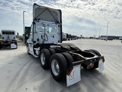 Rear/side angle view of a 2020 Freightliner PT126064S T tractor cab showing dual rear axles, fifth wheel area, and mud flaps with Brown tag; signage and lot in background.