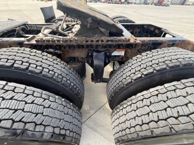 Truck rear view showing dual rear axles and fifth-wheel hitch on a Freightliner cab chassis with dual tires and rusty components visible.