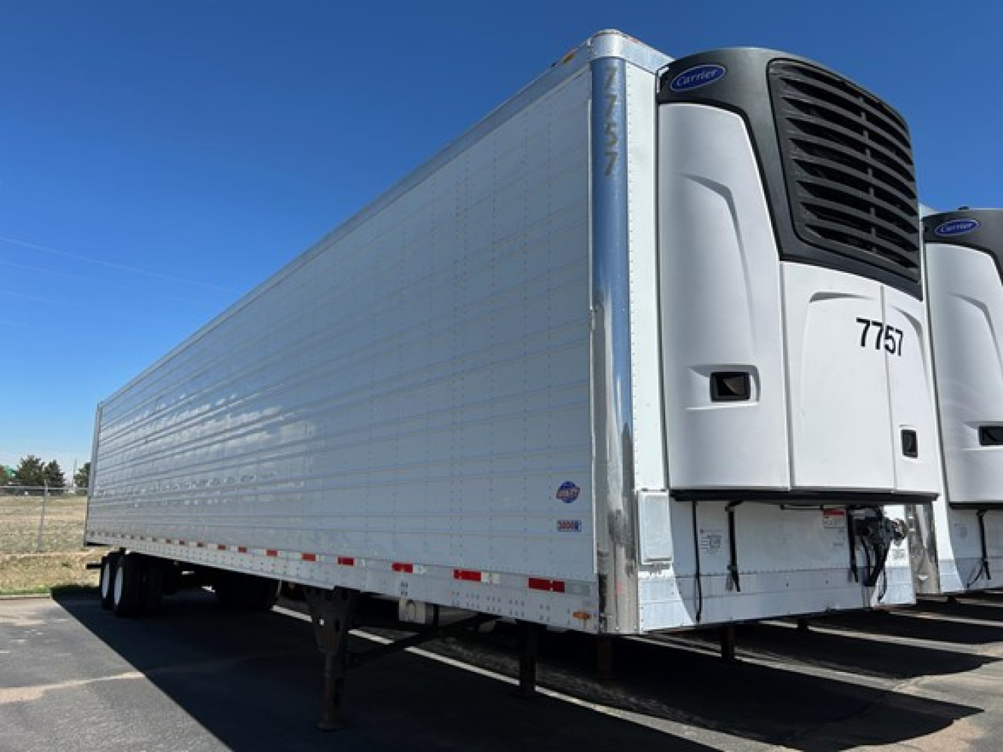 Trailer side and unit showing Thermo King reefer unit with '7757' on front, white insulated trailer, blue sky.