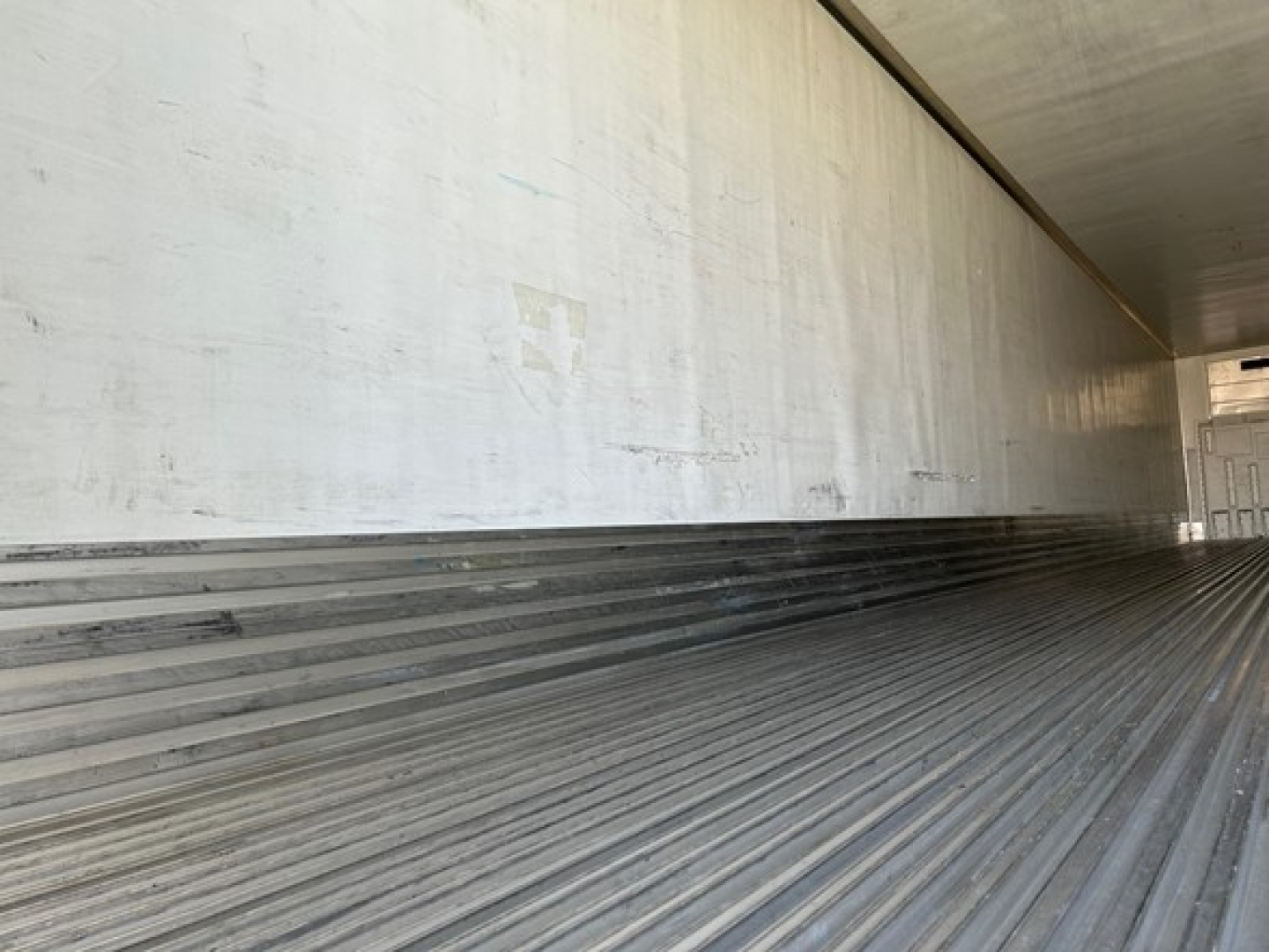 Trailer interior showing ribbed aluminum floor and smooth side walls with light from open end
