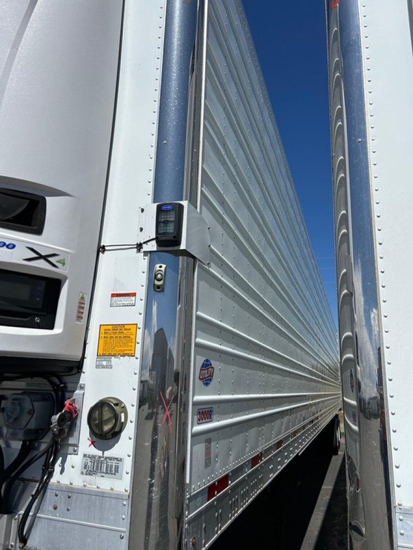 Truck trailer side with vertical refrigeration unit and doors; visible labels: various warning stickers, circular gauge, and a smallbox sensor on the door edge; chrome riveted panels