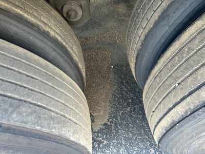 Rear dual-axle trailer tires with a view of the muddy ground between the wheels and a portion of the trailer frame.