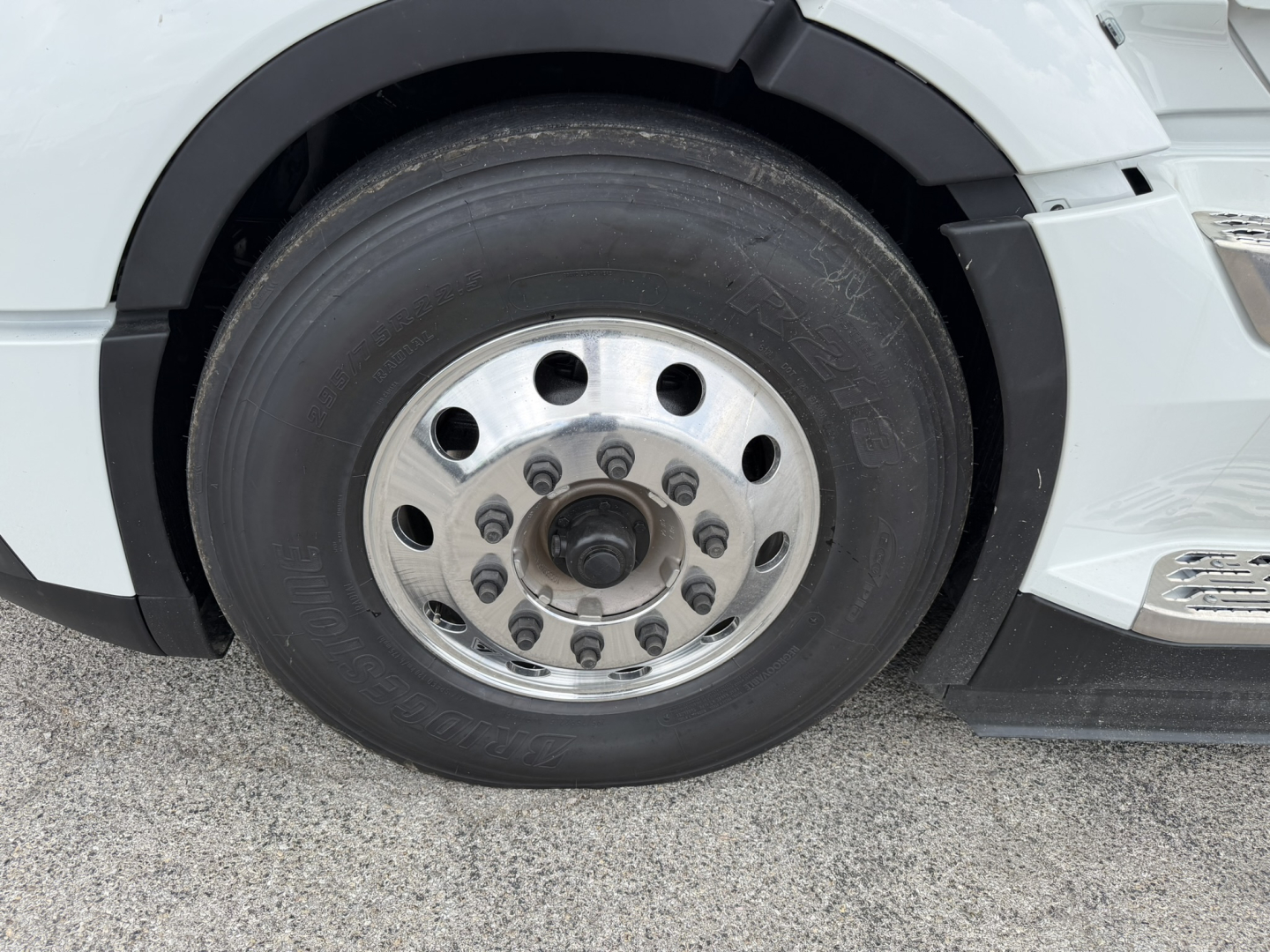 Wheel and tire close-up on a white Volvo VNL truck showing front axle with polished aluminum wheel and hub with multi-bolt pattern.