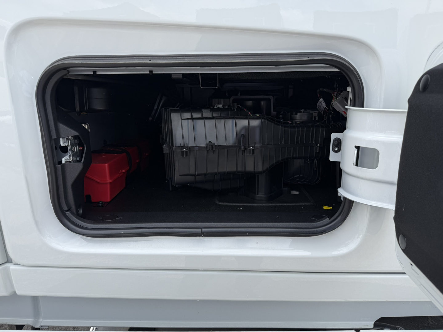 Truck side fuel/equipment bay view showing engine bay components and a red battery on the left.