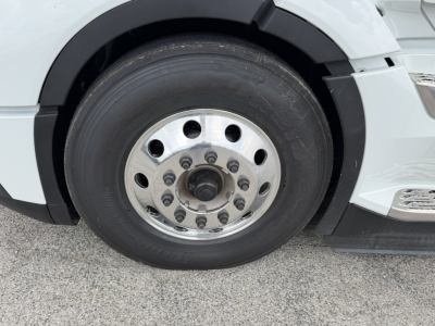 Wheel and tire close-up on a white Volvo VNL truck showing front axle with polished aluminum wheel and hub with multi-bolt pattern.