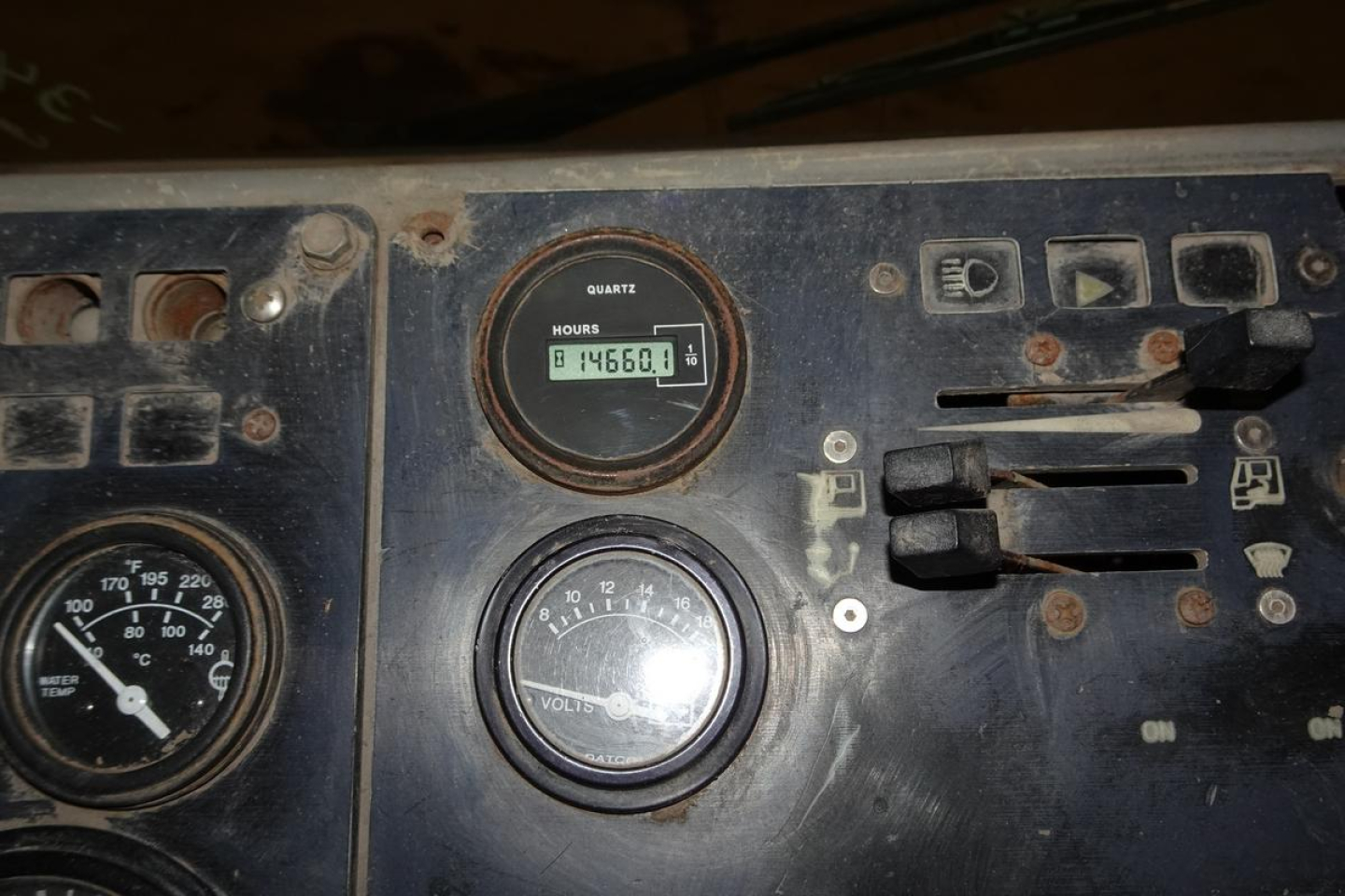 Dashboard panel of a used truck showing an hour meter reading 84560.1 hours, a voltmeter, and various switches in a dusty, worn control cluster.