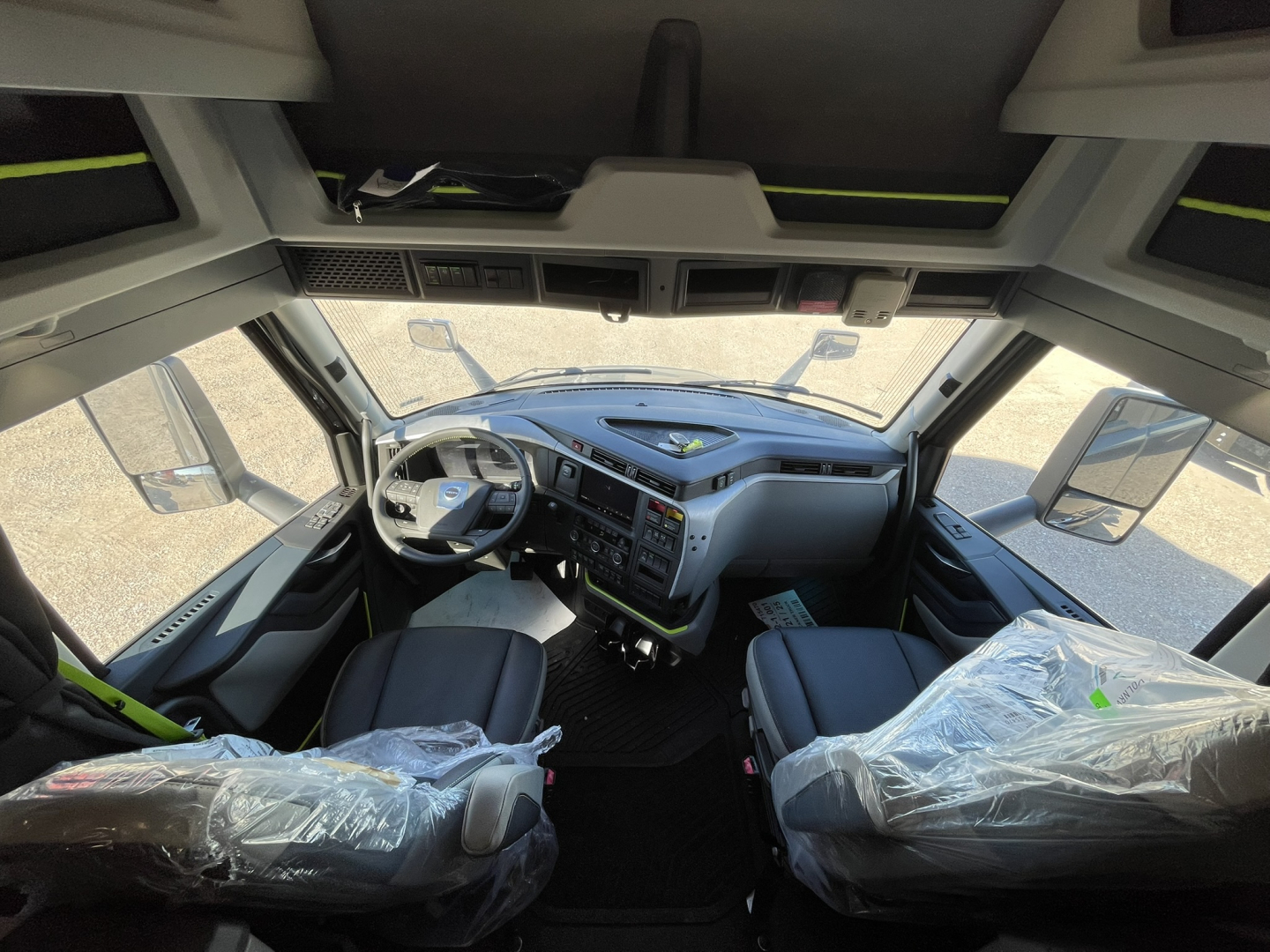 Volvo VNL cab interior showing steering wheel, dashboard, and driver/passenger seats wrapped in plastic; controls and windshield visible.
