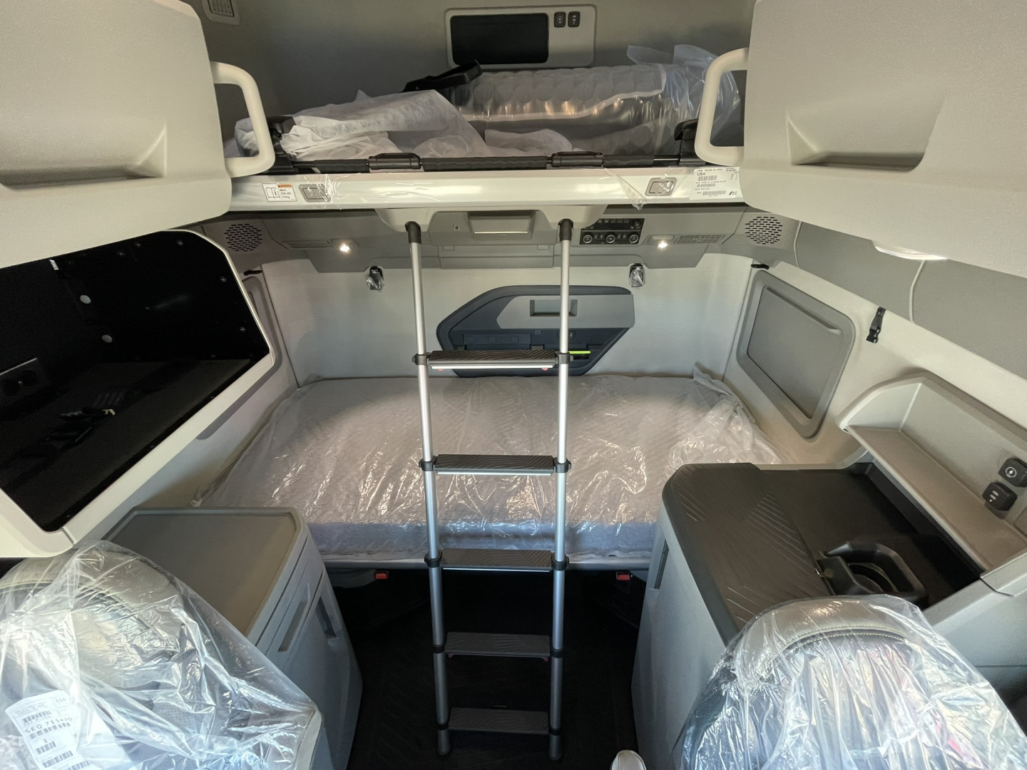 Volvo VNL64T860 sleeper cab interior with bunk bed area and compact ladder, storage compartments, and plastic-covered seats.