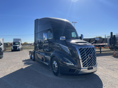 Volvo VNL64T860 truck in a sale lot, front three-quarter view, glossy dark blue exterior, large grille, sleeper cab, chrome mirrors.