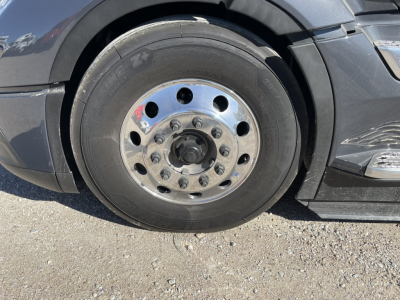Volvo heavy truck front wheel showing steel rim with multiple lug nuts and black tire. No visible text on tire; wheel well and side panel visible.