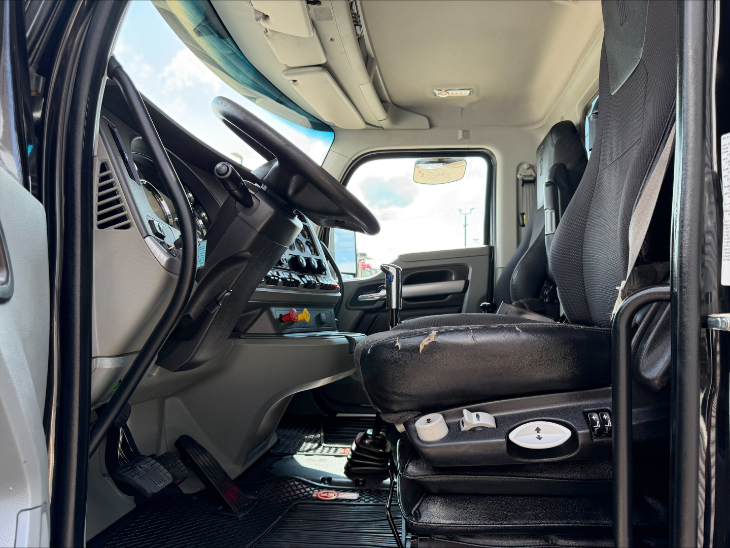 Kenworth T880 truck cabin interior showing driver seat, dashboard, steering wheel, and gear shifter with visible controls.