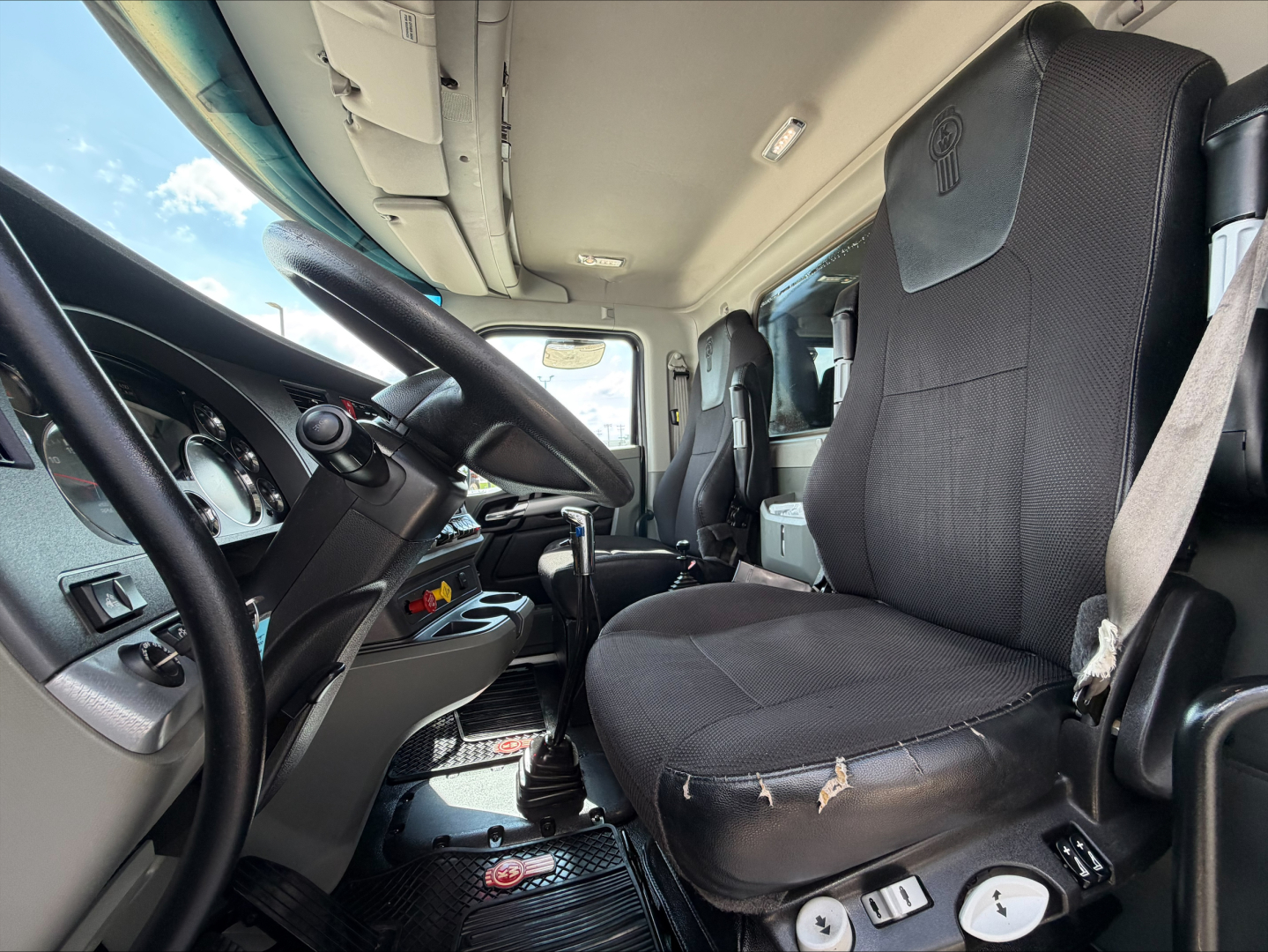 Kenworth T880 truck cabin interior showing driver seat and steering wheel with dashboard controls.