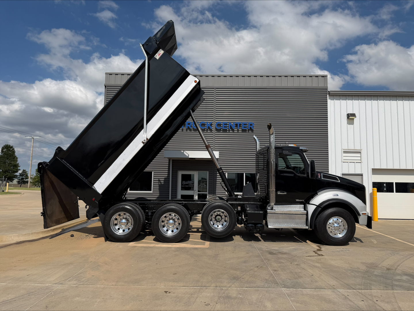 Kenworth T880 dump truck side profile with lifted bed showing six-wheel configuration and dump bed.