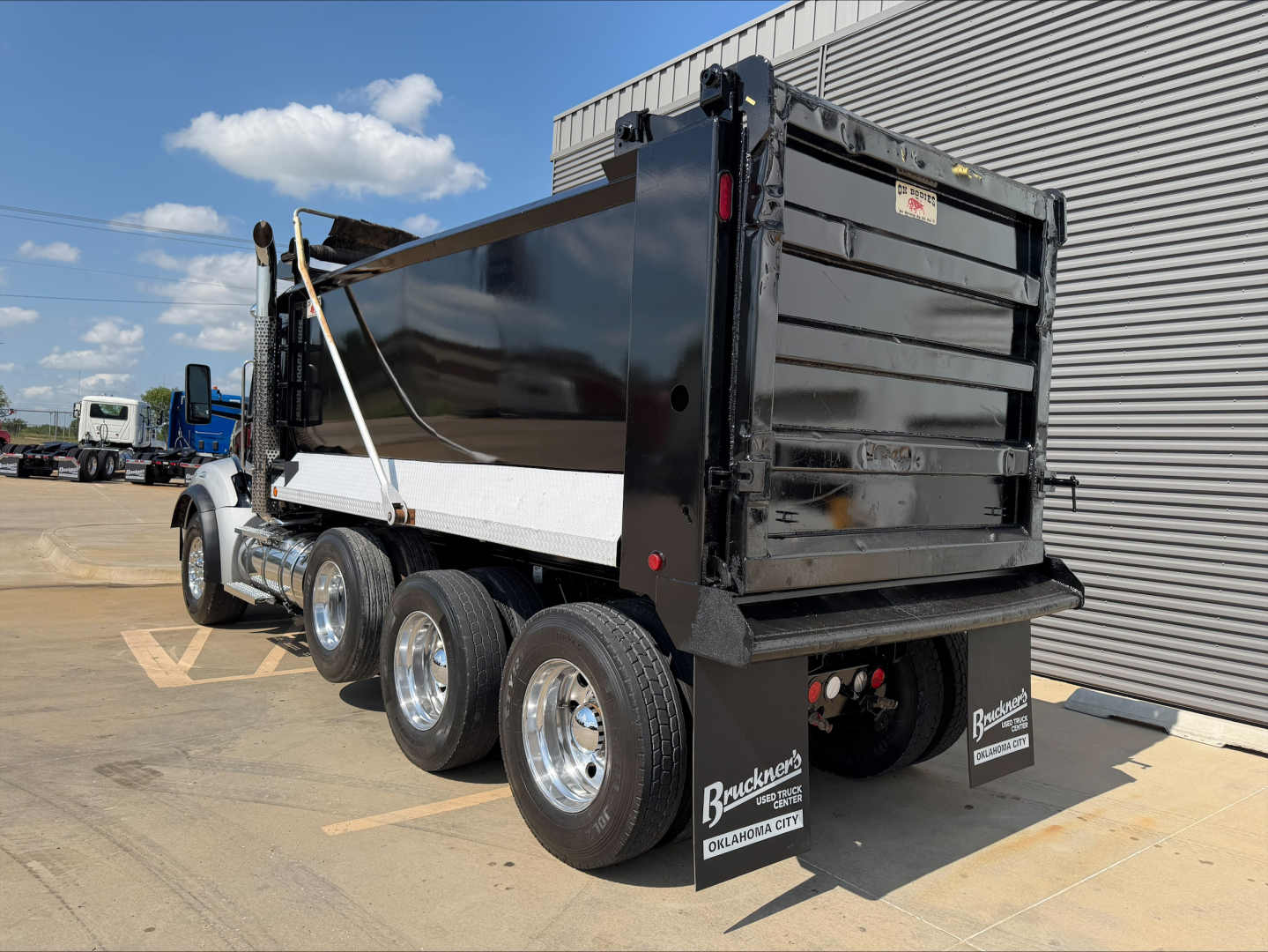 Kenworth T880 dump truck side/rear view showing black dump body and dual rear wheels, chrome wheels, white rails, and Ram PTO sticker; heavy-duty truck with multiple axles.
