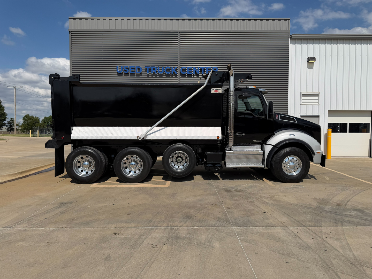 Kenworth T880 dump truck side view showing six-wheel configuration with black cab and white dump body, showroom lot in background.