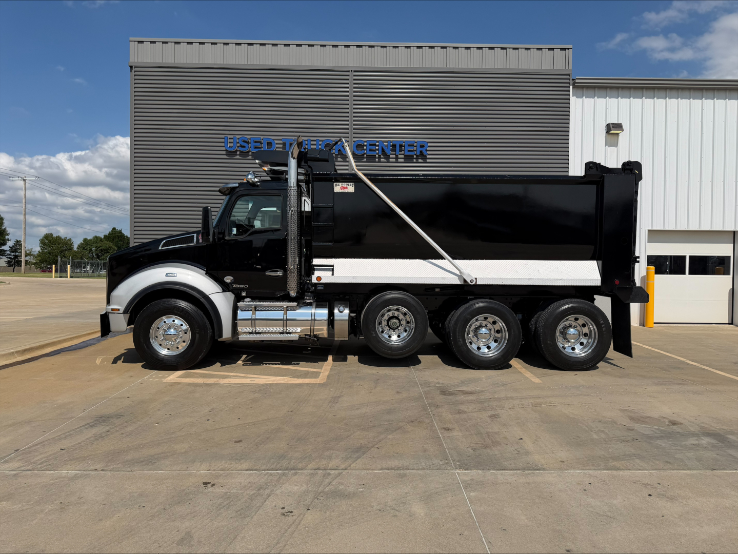 Kenworth T880 dump truck side view showing black dump body and gray cab with chrome steps.