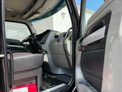 Truck cab interior of a 2020 Kenworth T880 showing the driver's seat, steering wheel, and dashboard area; front door open with light gray and black interior trim.