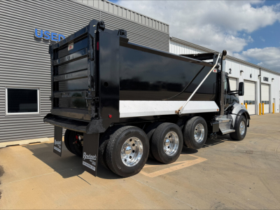 Kenworth T880 dump truck in service showing rear and side with black dump body and white side panel, dual rear axles, chrome wheels.