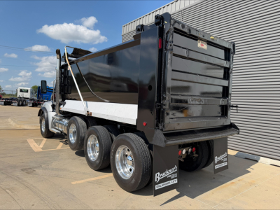 Kenworth T880 dump truck side/rear view showing black dump body and dual rear wheels, chrome wheels, white rails, and Ram PTO sticker; heavy-duty truck with multiple axles.