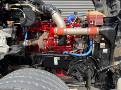 Kenworth T880 engine bay showing red engine block with blue and black hoses, silver exhaust pipe, and red coolant reservoir in front fender area.
