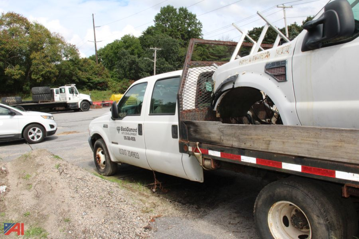 Ford F-350 Super Duty flatbed tow truck showing damaged front cab and tow body, white color with company logo and text on door