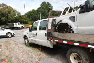Ford F-350 Super Duty flatbed tow truck showing damaged front cab and tow body, white color with company logo and text on door