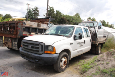 Ford F-350 Super Duty flatbed truck with utility bed and towing equipment, white cab, black grille, on a lot.