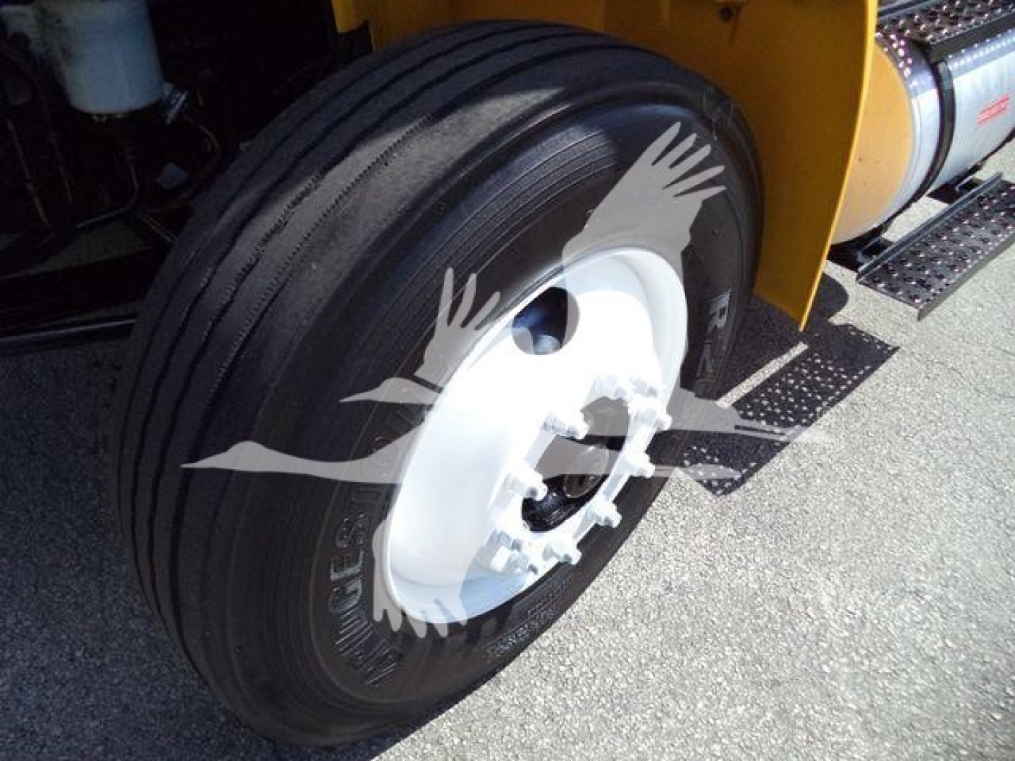 International 4300 dump truck wheel close-up showing large black radial tire mounted on white steel rim; part of yellow body and dump bed visible.