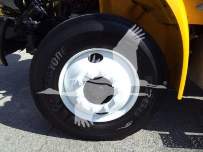 Truck wheel well and tire showing steel wheel, black tire with white rim; visible tire brand and letters; yellow bodywork in background.