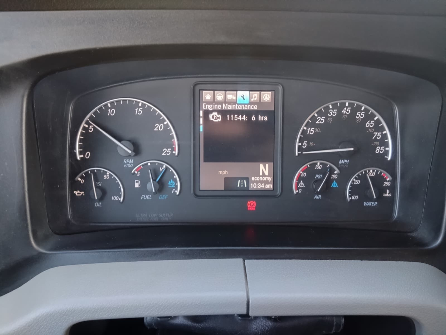 Dashboard view of a Freightliner Cascadia cab with gauge cluster, central digital display showing Engine Maintenance message, and various readouts.
