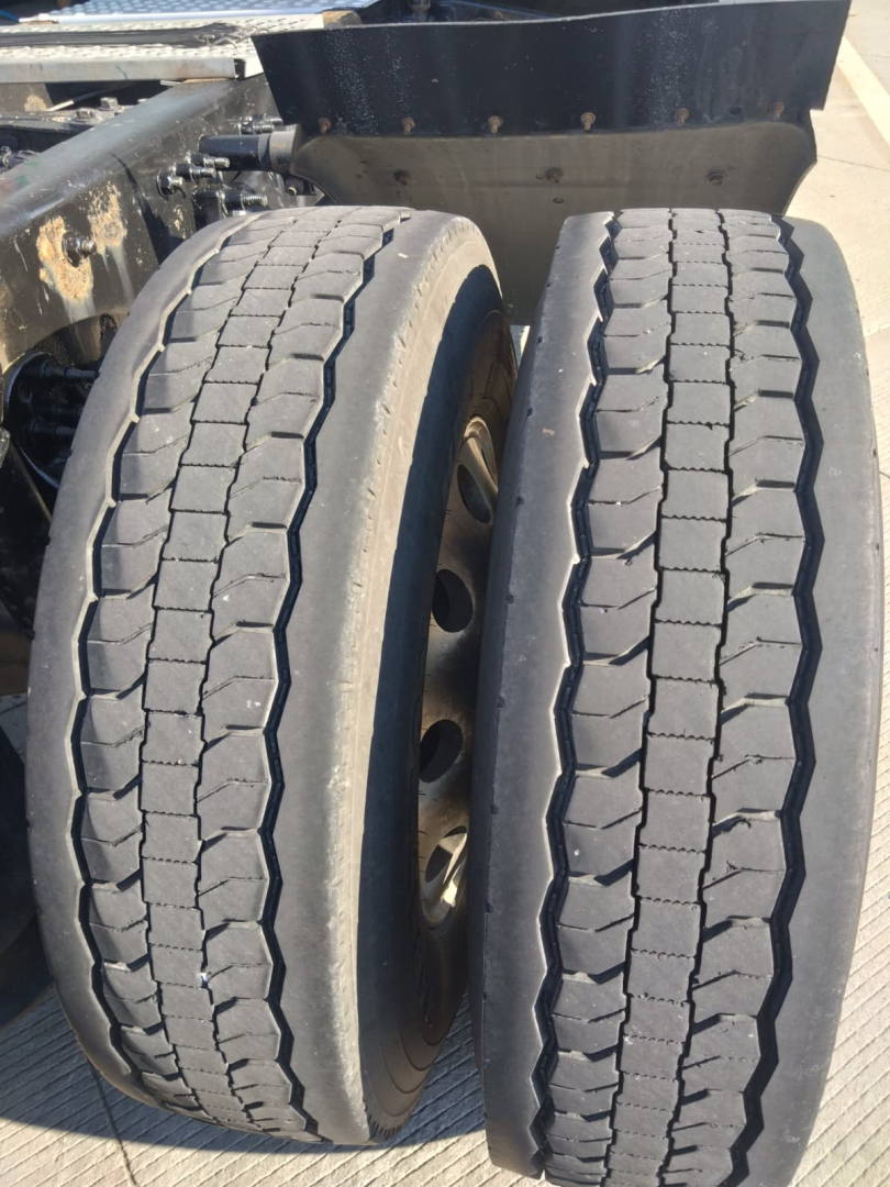 Truck dual rear tires with tread pattern visible; undercarriage and part of trailer/frame in view; wheel rims and suspension area visible