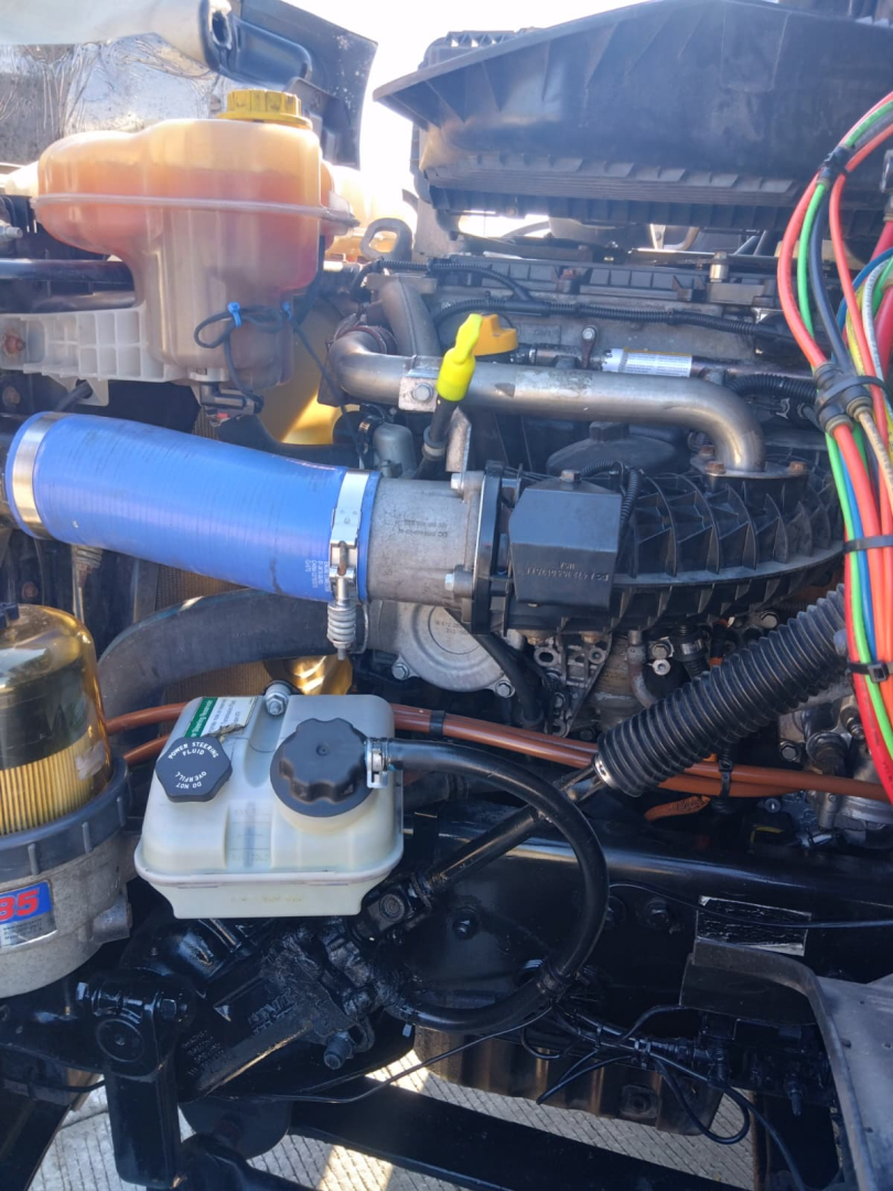 Truck engine bay showing coolant reservoir, various hoses, wiring harness, and intake components in a Freightliner CASCADIA.