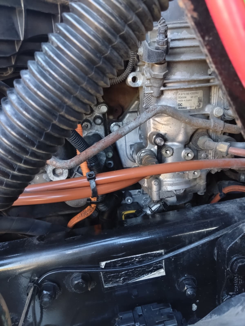 Engine bay of a 2020 Freightliner Cascadia showing fuel and electrical lines, aluminum engine block, hoses, and a metal tag with part numbers.
