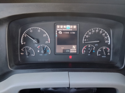 Dashboard view of a Freightliner Cascadia cab with gauge cluster, central digital display showing Engine Maintenance message, and various readouts.