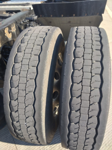 Truck dual rear tires with tread pattern visible; undercarriage and part of trailer/frame in view; wheel rims and suspension area visible