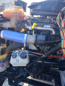 Truck engine bay showing coolant reservoir, various hoses, wiring harness, and intake components in a Freightliner CASCADIA.