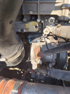Engine bay view from Freightliner Cascadia showing turbocharger and belts with hoses and metal components in view.