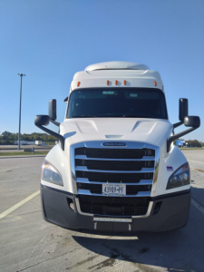 Front view of a white 2020 Freightliner Cascadia truck with large grille, daytime running lights, black bumper, and side mirrors; license plate visible.