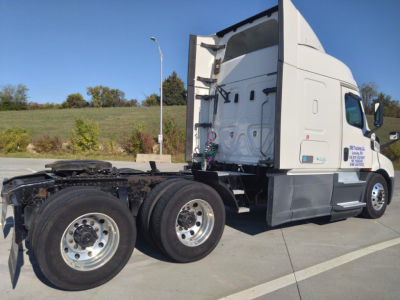 Truck cab and rear chassis of a Freightliner Cascadia sleepered tractor, side view showing tandem rear axles and primer white cab.