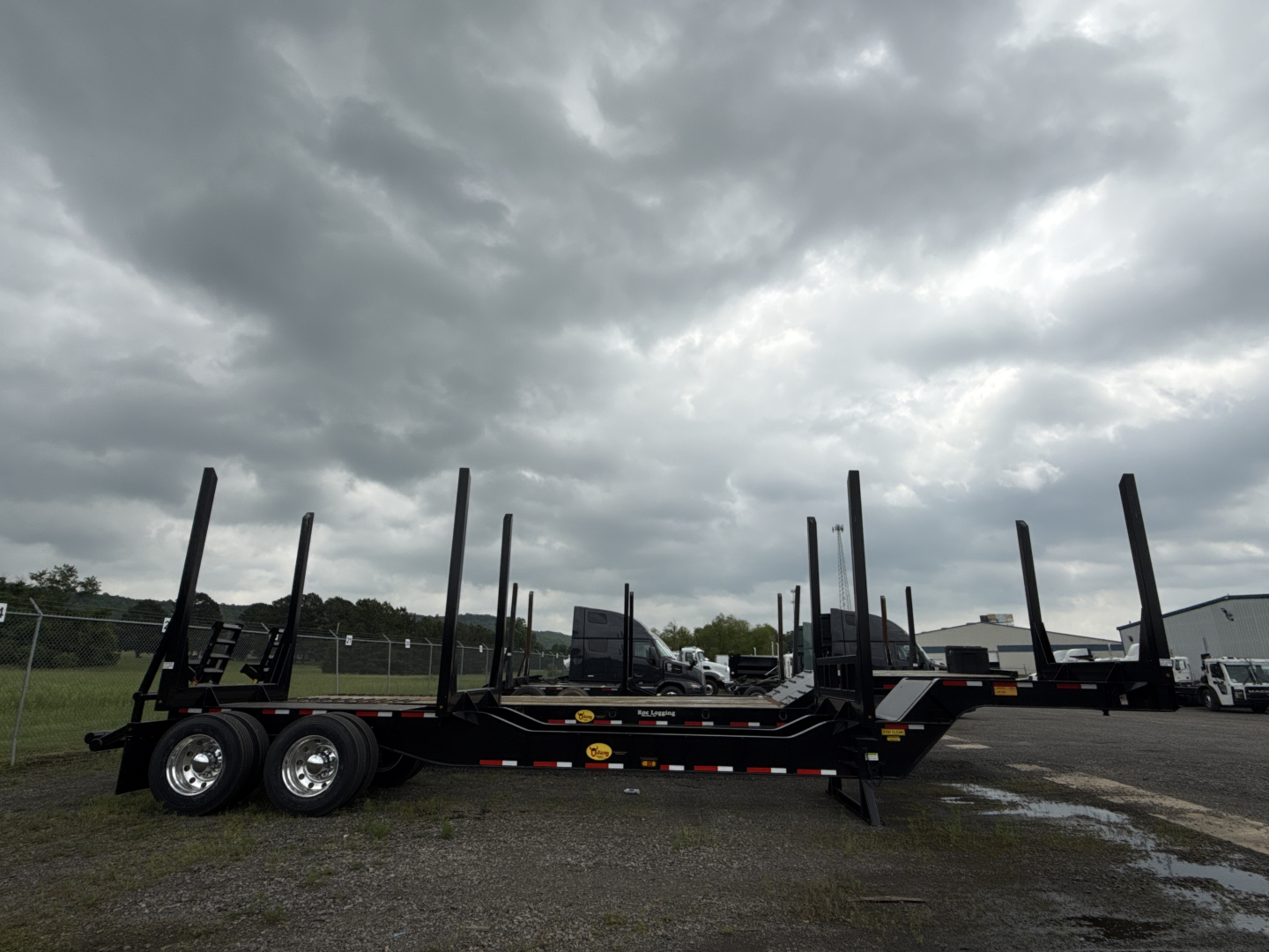 Trailer chassis with multiple vertical posts for log loading, dual rear axles, black steel frame, overcast sky.