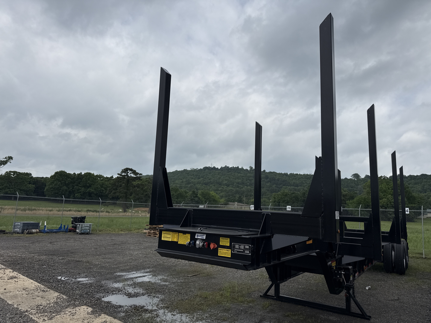 Trailer showing tall vertical stake beds for a Viking log trailer with a flatbed lower platform and dual axle in a field.