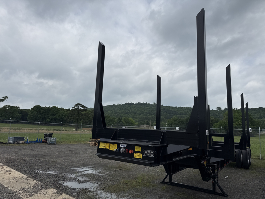 Trailer showing tall vertical stake beds for a Viking log trailer with a flatbed lower platform and dual axle in a field.
