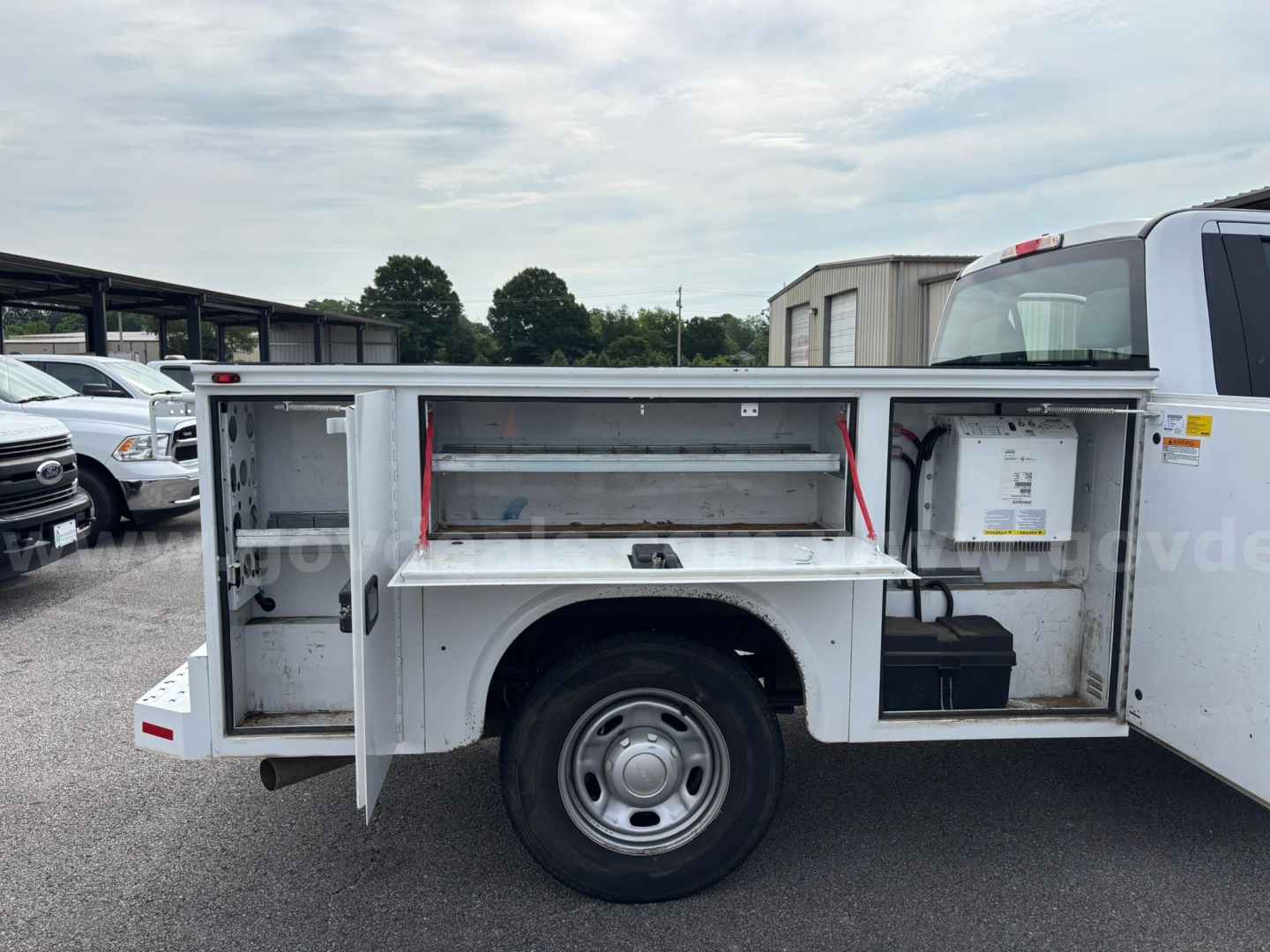 Utility truck side storage compartments open with shelving and tool area, Ford F-250 utility body, rear wheels visible.