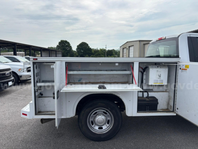 Utility truck side storage compartments open with shelving and tool area, Ford F-250 utility body, rear wheels visible.