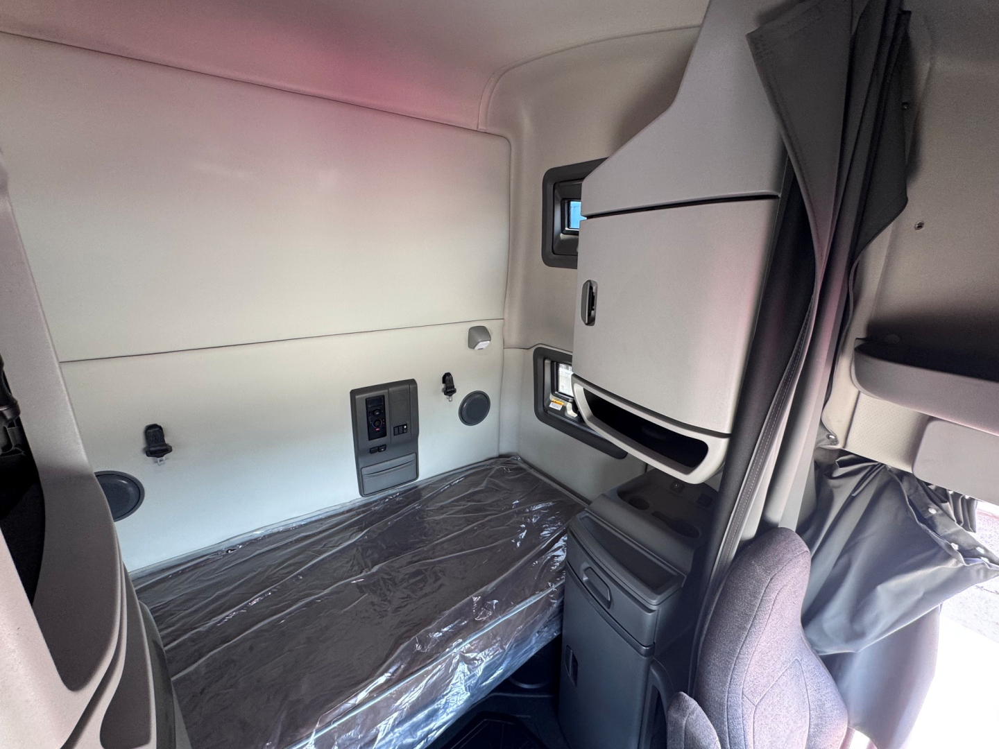Cabin interior of a 2021 Volvo VNL64T760 sleeper truck showing bunk area with plastic-wrapped mattress, side wall panels, storage compartments, and window.