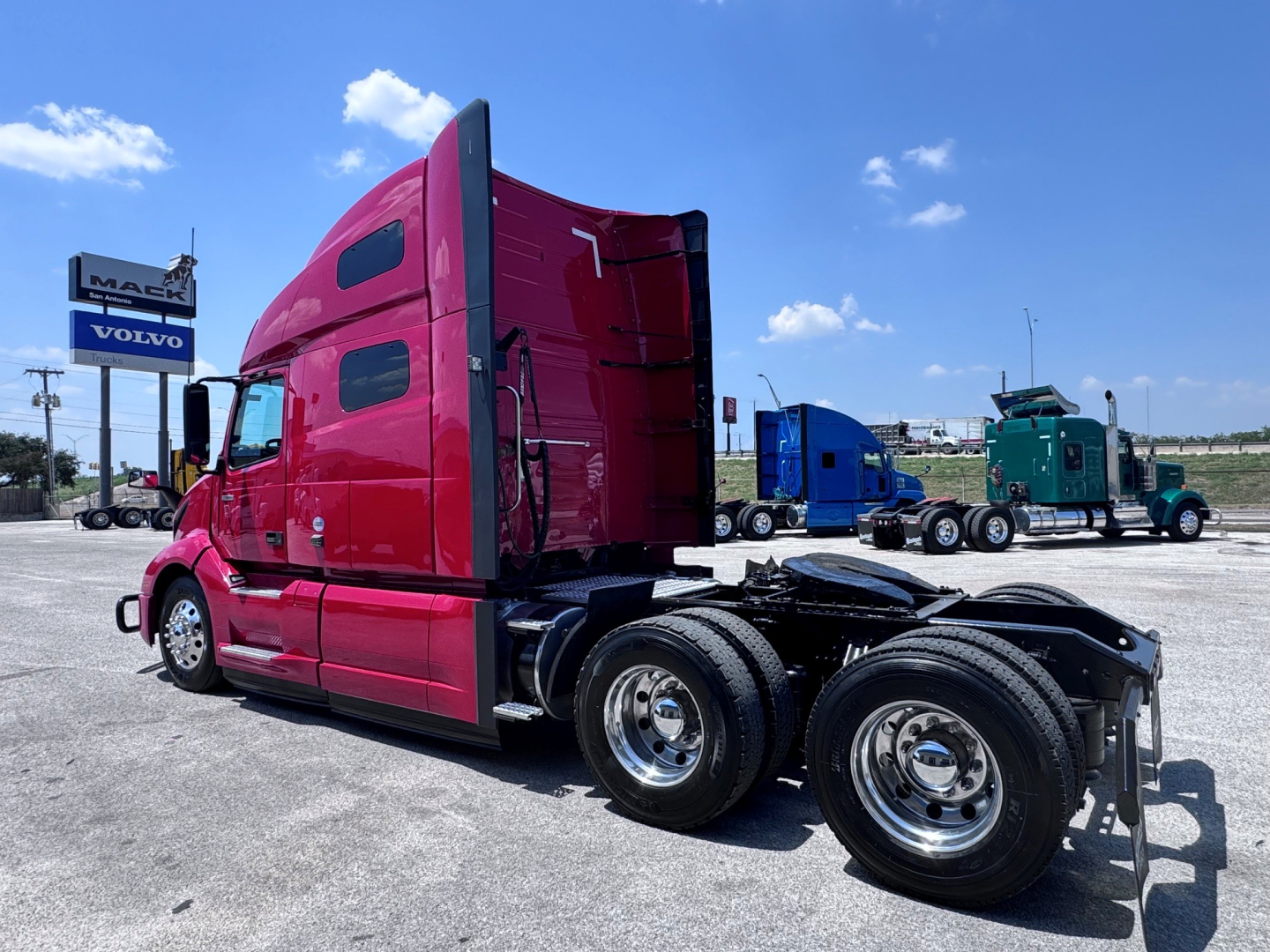 Semi truck tractor in red cab, side view showing sleeper and rear dual axles with chrome wheels.