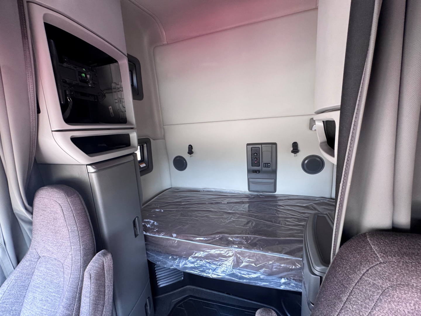 Cab interior of 2021 Volvo VNL64T760 sleeper showing bunk bed with plastic covering, side storage, dashboard switch panel, and windowed rear wall.