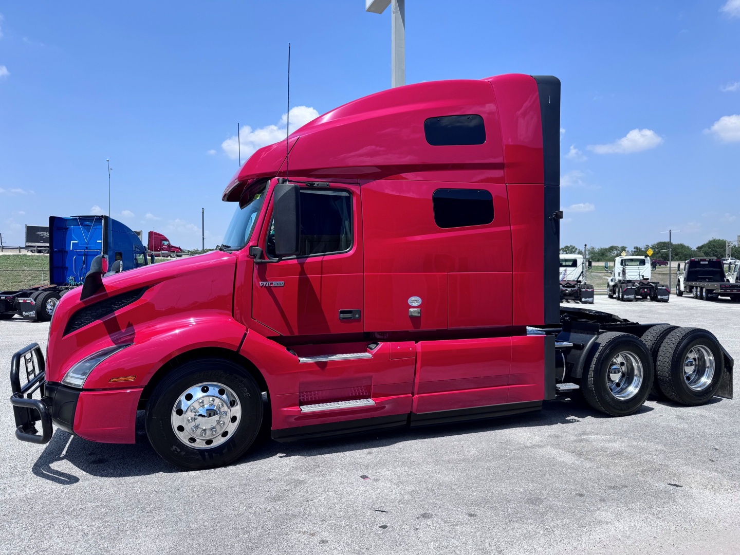 Volvo VNL64T760 sleeper cab tractor in red profile view showing driver door, front bumper, and dual rear axles.